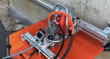 A construction worker using a concrete saw cuts asphalt and concrete curbs to create a track